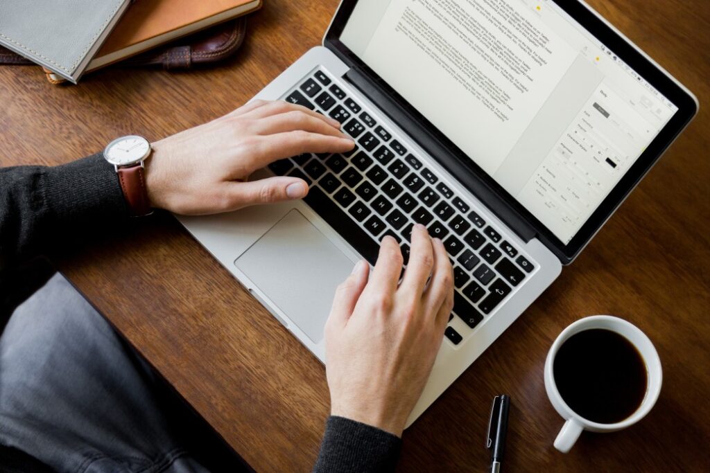 Man sitting at a wooden desk writing skills to resume using a laptop