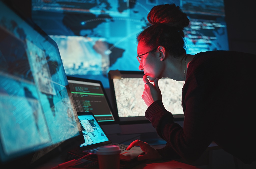 a woman using information technology to carefully monitor and manage digital defenses on multiple computer screens